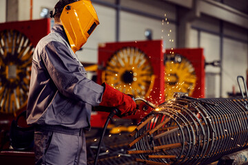 Wall Mural - A metallurgy worker welds metal framework with a welding machine in the factory.