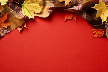 Wall Mural - Autumn background. Scarf and maple leaves on red table. Flat lay, top view, copy space. Autumn, fall concept.