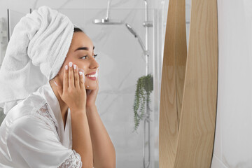 Wall Mural - Beautiful young woman applying cleansing foam onto face near mirror in bathroom, space for text. Skin care cosmetic