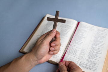 Wall Mural - Hand holding religious crucifix cross on top of Holy Bible. Christian faith and devotion concept. Copy space.