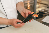 Fototapeta  - Chef hands cooking sushi with rice, salmon and nori on kitchen of japanese restaurant