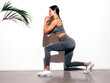 © halayalex - Tanned fitness woman in grey sports clothing. Sexy young smiling beautiful model with perfect body.Female isolated on white background in studio. Stretching out before training. Near wall