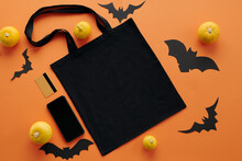 Top-down View Shot Of Flat Lay With Black Shopper Bag, Small Pumpkins, Smartphone, Paper Bats And Bank Card On Orange Surface