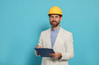 © New Africa - Professional engineer in hard hat with clipboard on light blue background