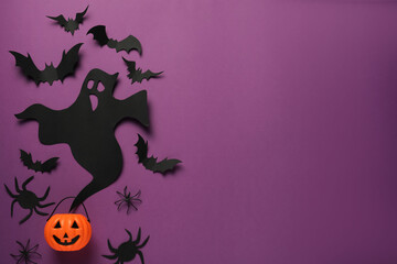 Wall Mural - Flat lay composition with paper ghost, bats and plastic pumpkin basket on purple background, space for text. Halloween celebration