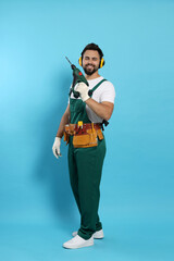 Wall Mural - Young worker in uniform with power drill on light blue background