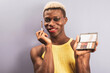 An african boy posing on a purple background while showing cosmetics, androgynous concept.