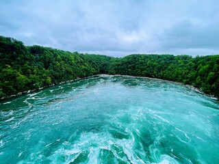 High-angle closeup of a Niagara Whirlpool with flowing water, green trees on both sides