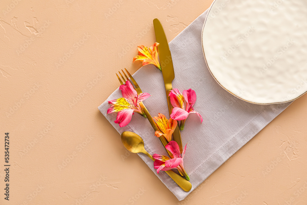 Table setting with plate, cutlery and alstroemeria flowers on beige background