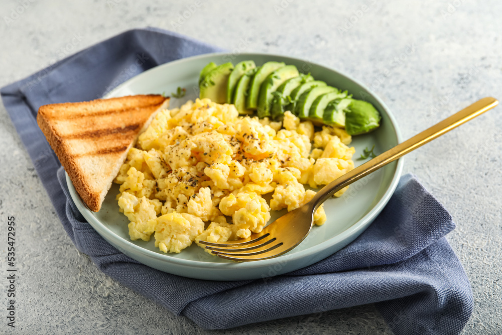 Plate with tasty scrambled eggs, avocado and toast on light background