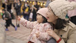 taiwanese mother and baby smiling with joy while having fun watching dancing fountain on a city square with group of tourists taking photos at background
