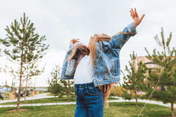 A little girl with long hair jumps having fun on the street. The concept of a happy childhood.