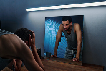 Wall Mural - young insomniac man holding head in hands in front of mirror with reflection of him expressing anger