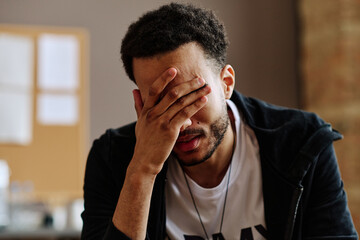 Wall Mural - Young depressed man touching face while suffering from post traumatic syndrome and describing his problems at psychological session