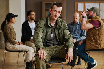 Wall Mural - Young Caucasian man with post traumatic syndrome sitting in front of camera on background of intercultural people from support group