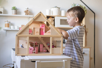 Wall Mural - Cute male kid playing toy doll house with interior furniture Montessori wooden eco friendly material