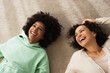 © LIGHTFIELD STUDIOS - top view of happy african american girl smiling while lying on carpet with cheerful mother.
