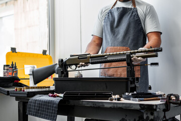 Wall Mural - Close up of young man in apron disassembling a gun above the table