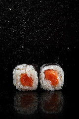 Poster - Sushi rolls with rice and salmon on a black background with reflection and splashes of water
