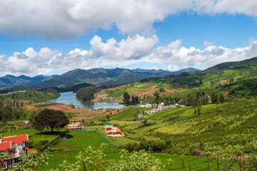 Wall Mural - Towering mountains, river with visible small houses, blue and white sky, reflection visible in water, nature's gift of greenery everywhere is the way one can explain the beauty of Ooty.