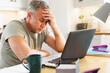 © Wavebreak Media - Thoughtful caucasian man sitting at table in kitchen and using laptop