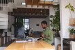 © wavebreak3 - Happy african american man sitting at table in kitchen using laptop and smartphone