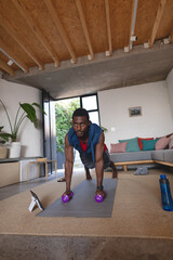 Wall Mural - Happy african american man exercising, using tablet in living room