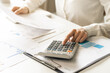 © KMPZZZ - Account finance, asian young business woman hand use calculator for calculate budget, cost and income of company from bills, reports paperwork, plan spend money expenses, working on desk at home.