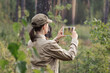 A woman forester in uniform take a photo using a digital tablet in a forest area in summer, back view, selective focus.