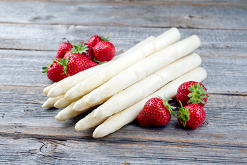 Reife rote Erdbeeren und weißer Spargel aus biologischem Anbau angeboten als close-up auf einem rustikalen alten Holz Board