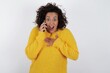 © Roquillo - Smiling young beautiful woman with curly short hair wearing yellow sweater over white background  talks via cellphone, enjoys pleasant great conversation. People, technology, communication concept