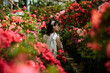 A girl in a light brown dress and glasses in a garden of blooming azaleas