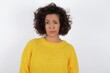 Displeased young beautiful woman with curly short hair wearing yellow sweater over white background frowns face feels unhappy has some problems. Negative emotions and feelings concept