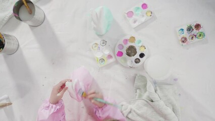 Sticker - Flat lay. Little girl painting paper mache figurine at homeschooling art class.