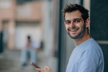 Wall Mural - attractive young man with beard smiling on the street with mobile phone