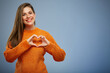 Smiling woman in warm orange sweater making heart with finger.