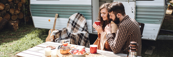 Wall Mural - Young beautiful loving couple travelling across country in the van. Millennial man and woman in a travel camper. Cozy atmosphere, vacations vibe. Banner copy space