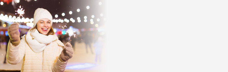 Banner smiling young woman wearing winter knitted clothes holding sparkler outdoors over snow background copy space. Christmas holidays.