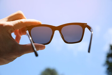 Poster - Mature man holding stylish sunglasses outdoors on sunny day, closeup