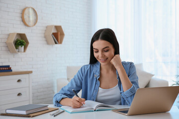 Poster - Young woman taking notes during online webinar at table indoors