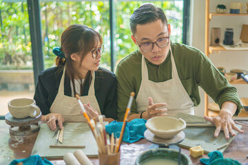 Focus couple potter working on potters wheel making ceramic pot from clay in pottery workshop. Couple in love working together in potter studio workshop.