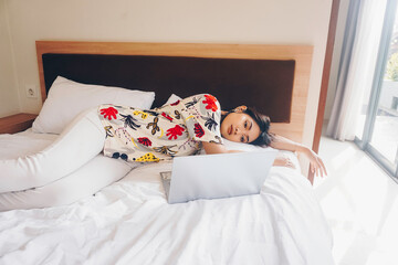 Wall Mural - A sleepy young woman yawning while working from the bed.