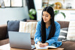 © kucherav - Woman student studying remotely using a laptop, taking notes on notepad sitting from home during online lesson, e-learning concept