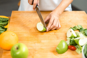 Wall Mural - Hand of slicing and cooking green apple on cutting board for vegetable salad in weight loss diet. Beautiful woman happily cooks a healthy breakfast in kitchen in the morning. Diet food concept.