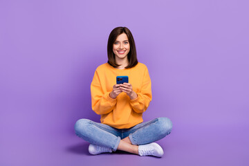 Wall Mural - Full body photo of young adorable businesswoman sitting chilling using her smartphone successful influencer isolated on violet color background