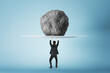 Success, power and strength concept with businessman back view holding huge stone. above his head, feeling tired on blue background
