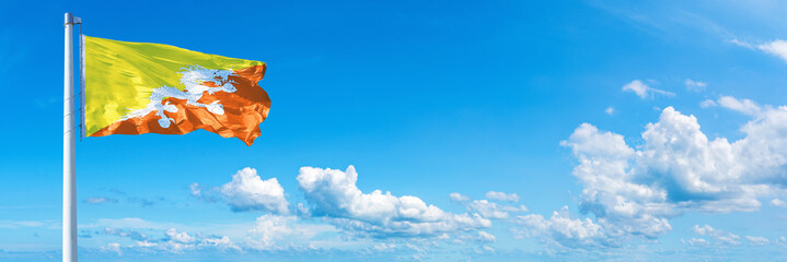 Wall Mural - Bhutan flag waving on a blue sky in beautiful clouds - Horizontal banner