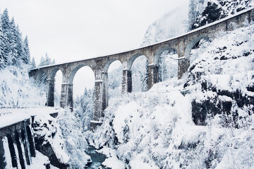  Mountain landscape with Sainte Marie bridge covered with snow in Les Houches, Chamonix valley, Eastern France. Viaduct bridge built to carry a railway over water.
