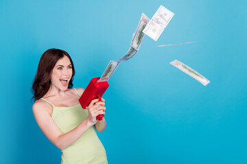 Sticker - Photo of cool excited girl dressed green clothes shooting money gun looking empty space isolated blue color background