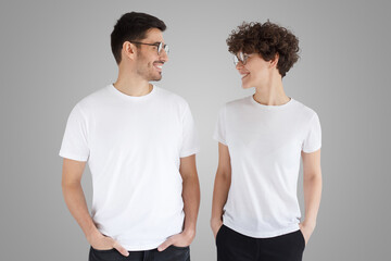 Wall Mural - Smiling couple in white t-shirts looking at each other, isolated on gray background